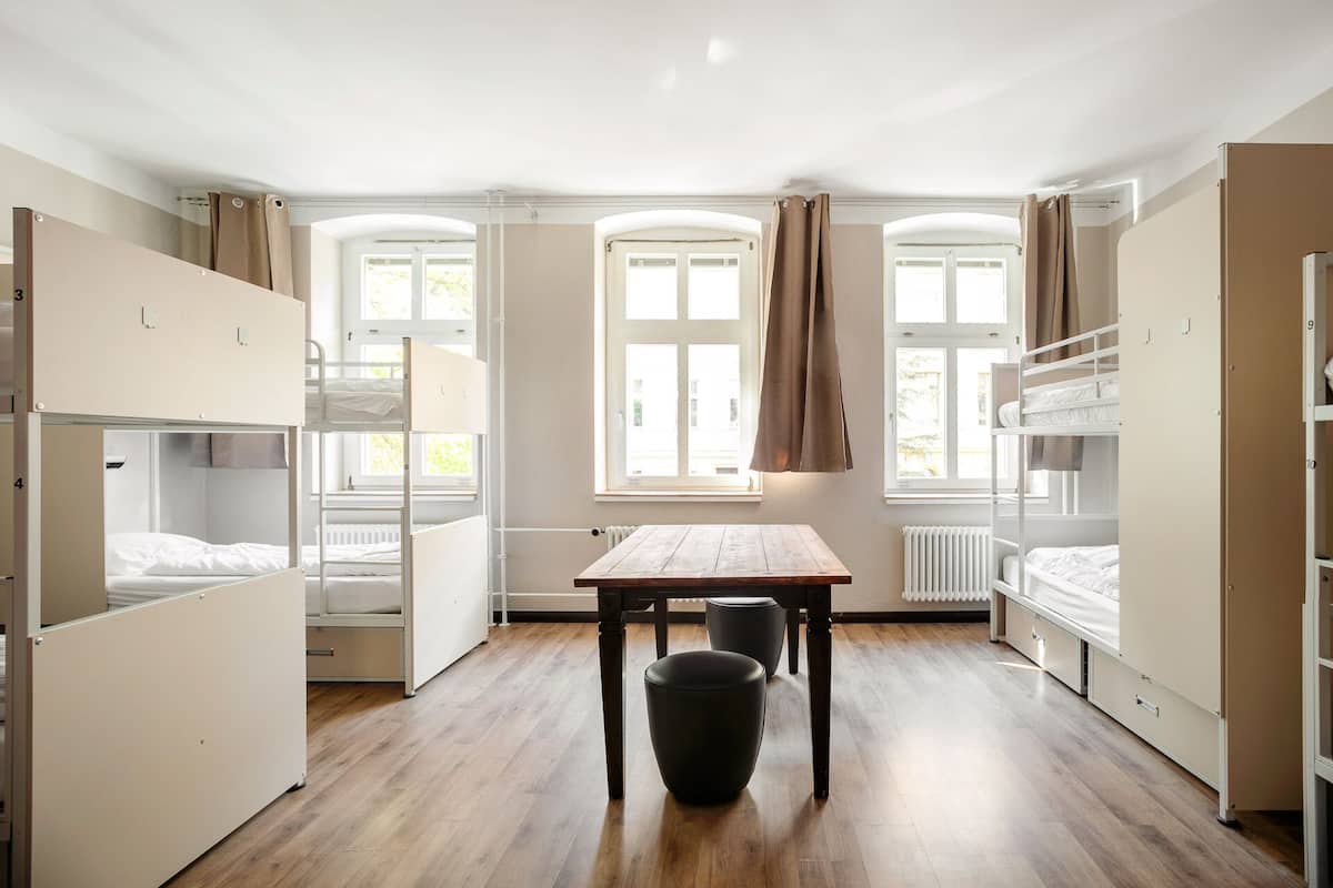 A dormitory room with bunk beds, a wooden table, and a radiator.