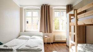 A bedroom with a bed, a wooden bunk bed, a radiator, and windows with curtains. - EastSeven Berlin Hostel (Berlin)