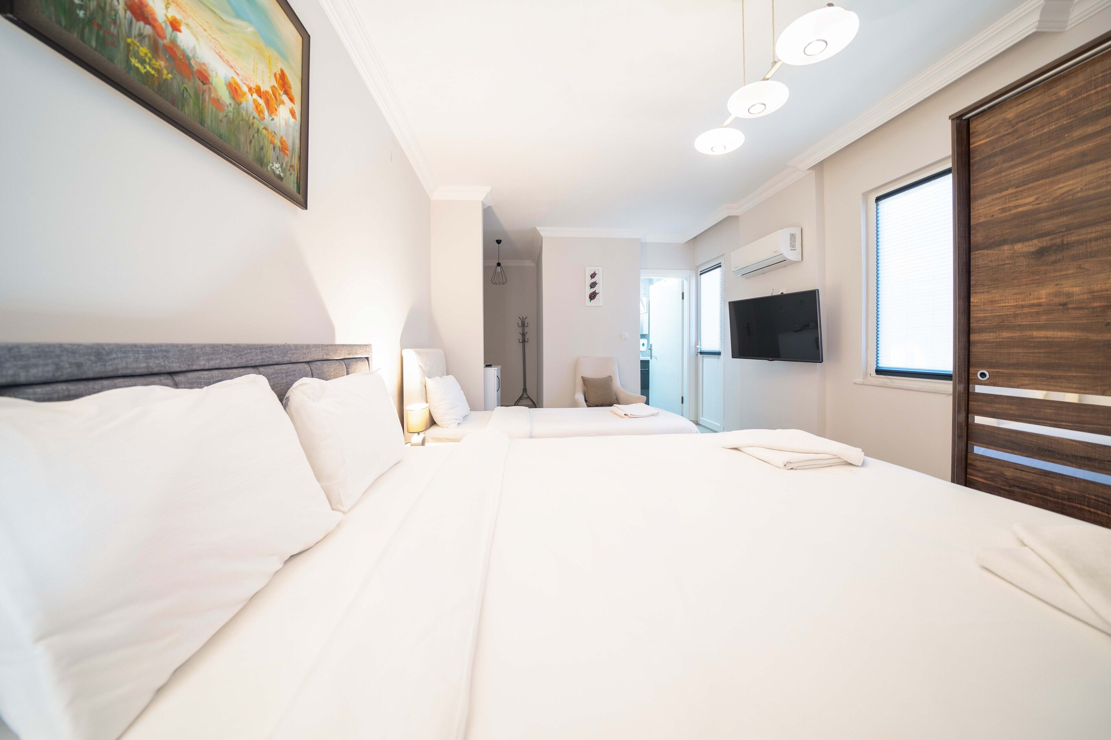 A hotel room with a large bed, a TV, a wooden wardrobe, and a painting on the wall.
