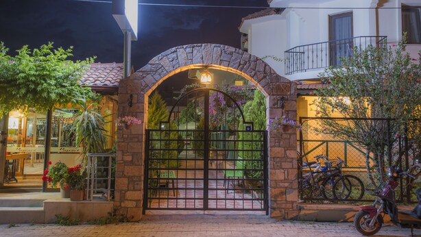 A stone archway leading to a gated entrance, a motorcycle parked outside, and a building with a balcony. - Dedeminn Garden Hotel (Fethiye)
