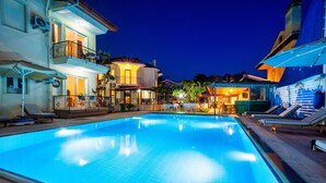 A swimming pool with lounge chairs and umbrellas, surrounded by buildings with balconies and outdoor seating areas. - Dedeminn Garden Hotel (Fethiye)