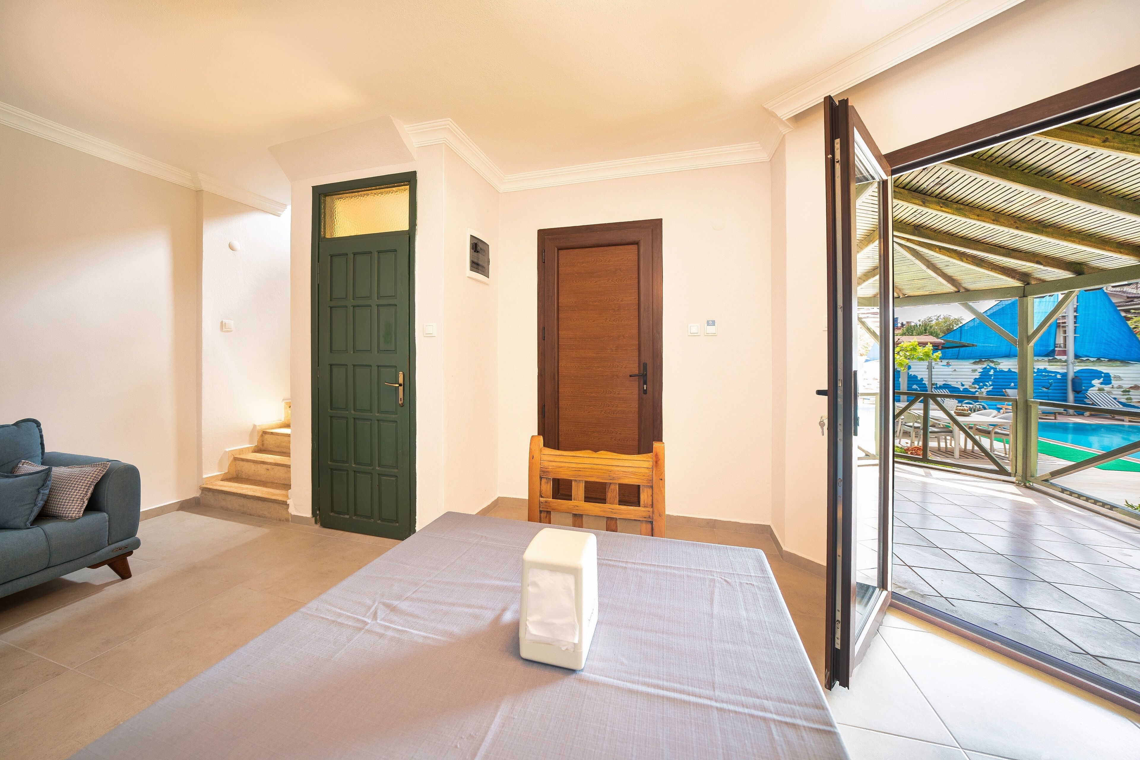 A room with a bed, a sofa, a wooden chair, and a sliding glass door leading to an outdoor pool area.