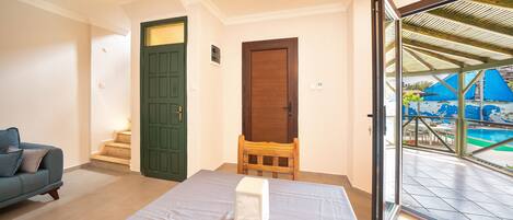 Una habitación con una cama, un sofá, una silla de madera y un ventanal corredero que da a una zona de piscina exterior.