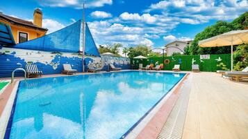 Una piscina con sillones de playa y sombrillas, rodeada por un muro verde con adornos náuticos.