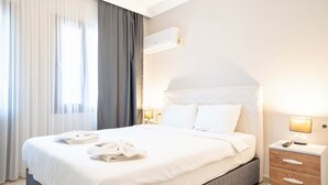 A neatly made bed with white linens, a bedside lamp, and a nightstand with a lamp. - Dedeminn Garden Hotel (Fethiye)