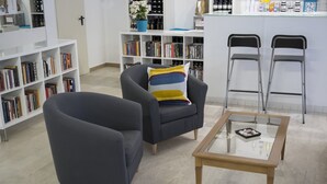 A modern library or reading area with a dark armchair, a glass-top coffee table, and two metal folding chairs. - Blue Sky (Rimini)