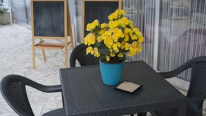 A table with a blue pot of yellow flowers, a small tray, and a chalkboard in a cafe setting. - Blue Sky (Rimini)
