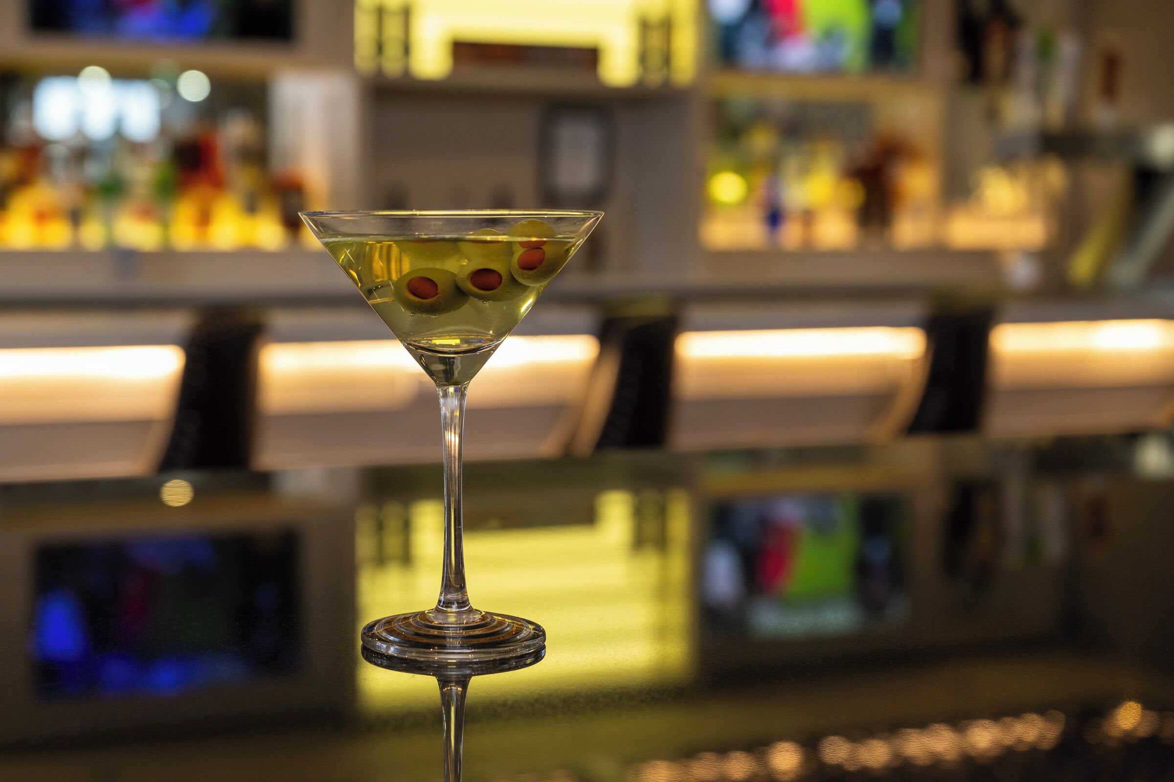 A martini glass with olives on a bar counter.