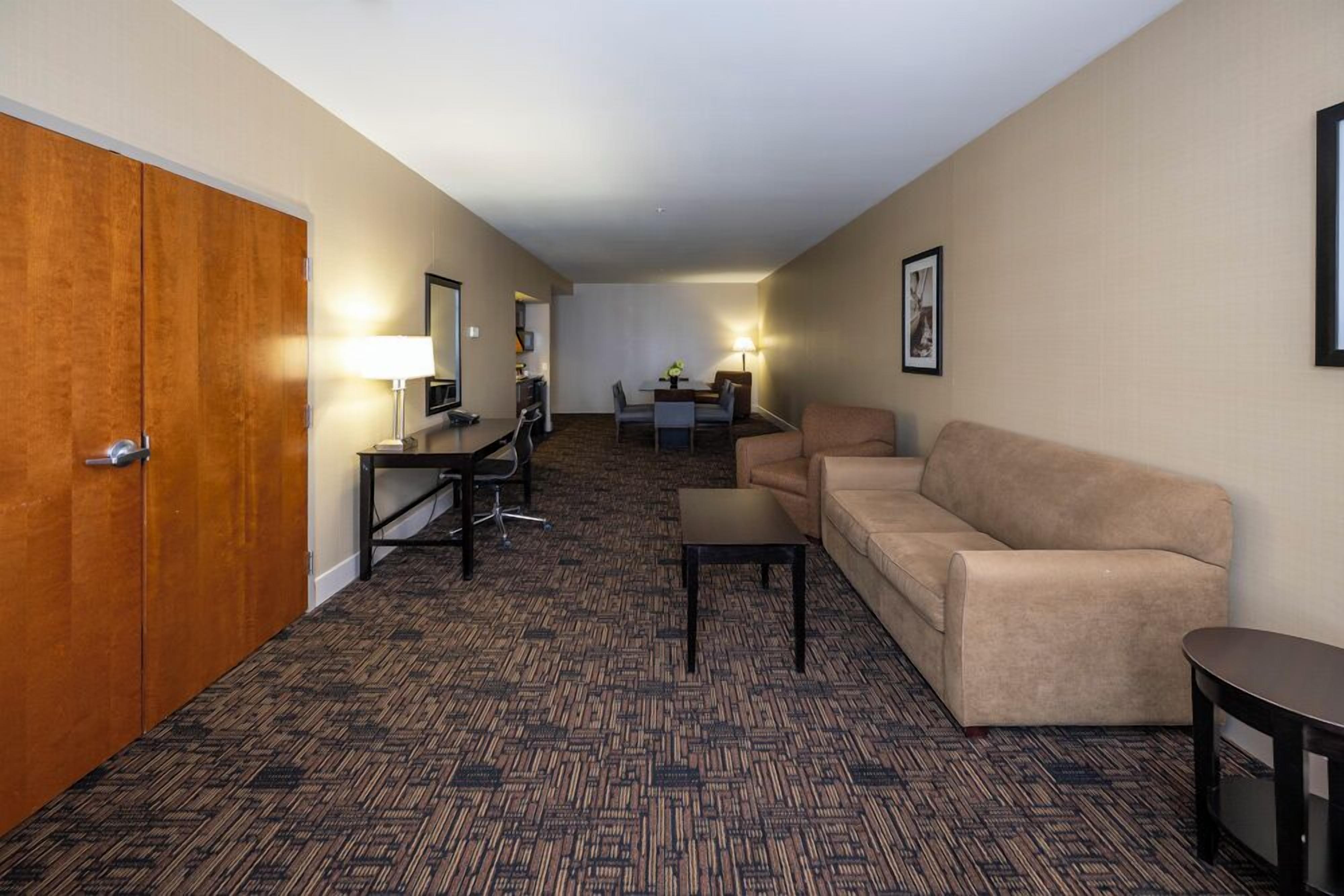 Habitación de hotel con piso alfombrado, sofá, escritorio con silla, televisión y armario.
