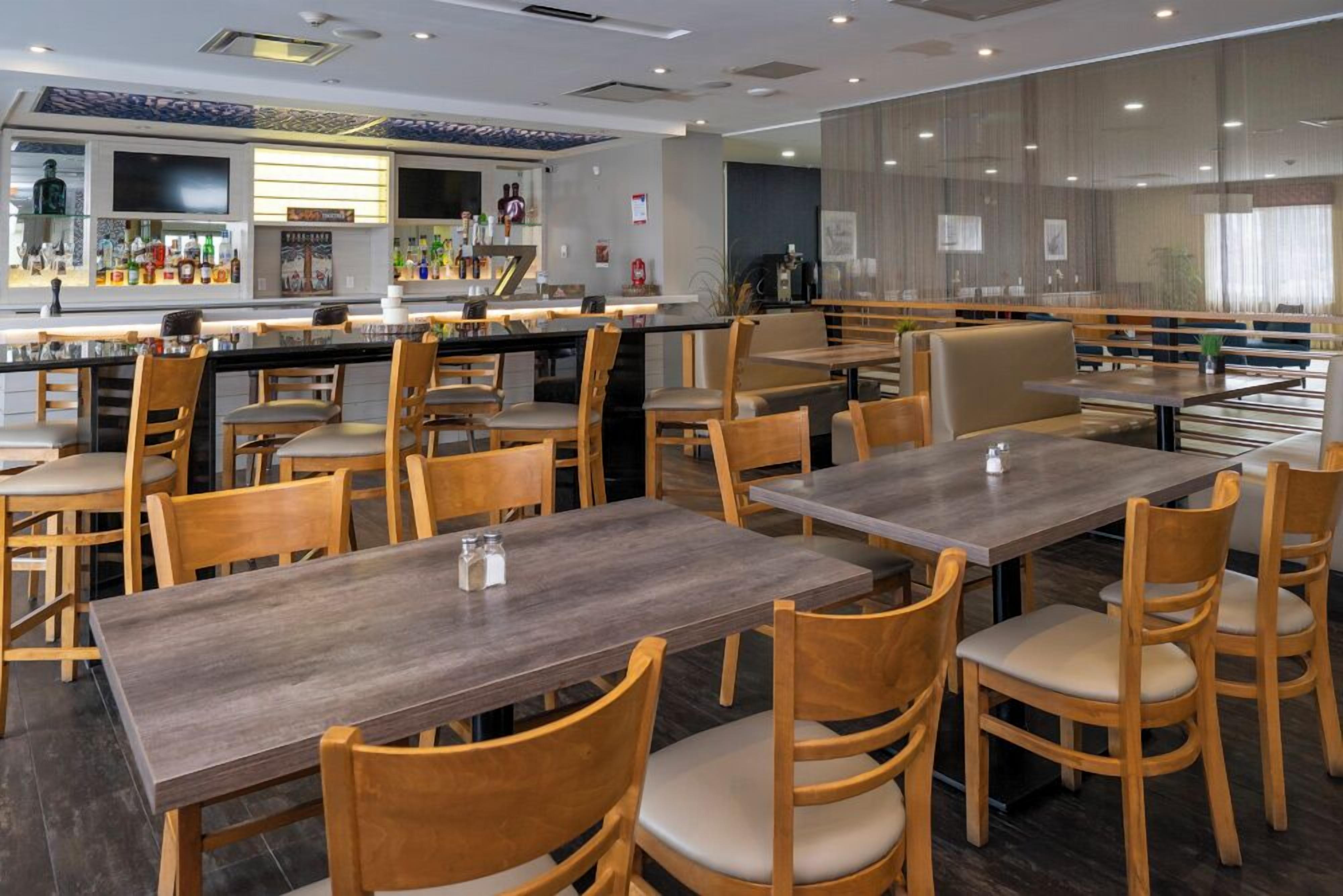 Un restaurant avec des tables et des chaises en bois, un coin bar et une vue sur la ville.
