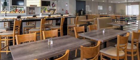 Un restaurante con mesas y sillas de madera, una zona de bar y vistas a la ciudad.