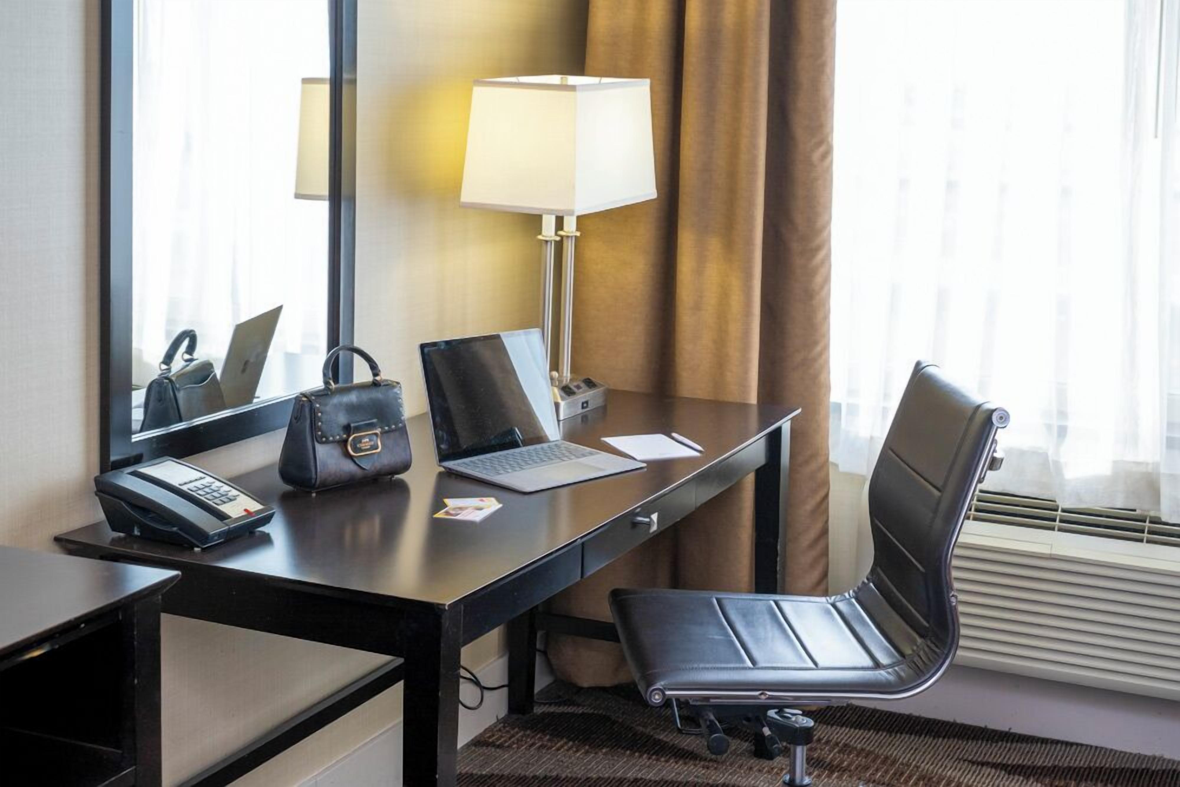 Una habitación de hotel con escritorio, computadora portátil, teléfono y una silla.