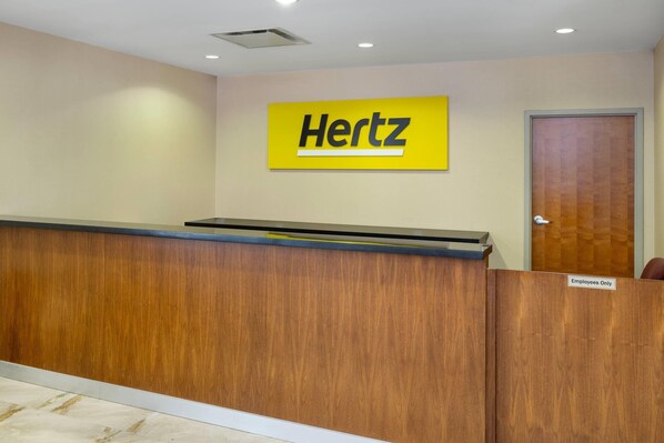 A reception desk with a 'Hertz' sign, a wooden counter, and a door marked 'Employees Only'.
