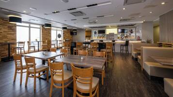 Un restaurante moderno con mesas y sillas de madera, una zona de bar y una cocina al fondo.