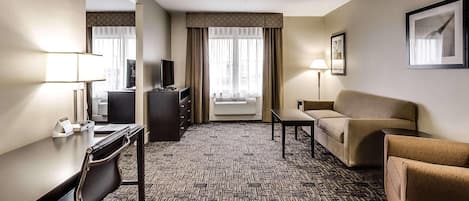 A hotel room with a desk, a chair, a sofa, a television, and a window with curtains.