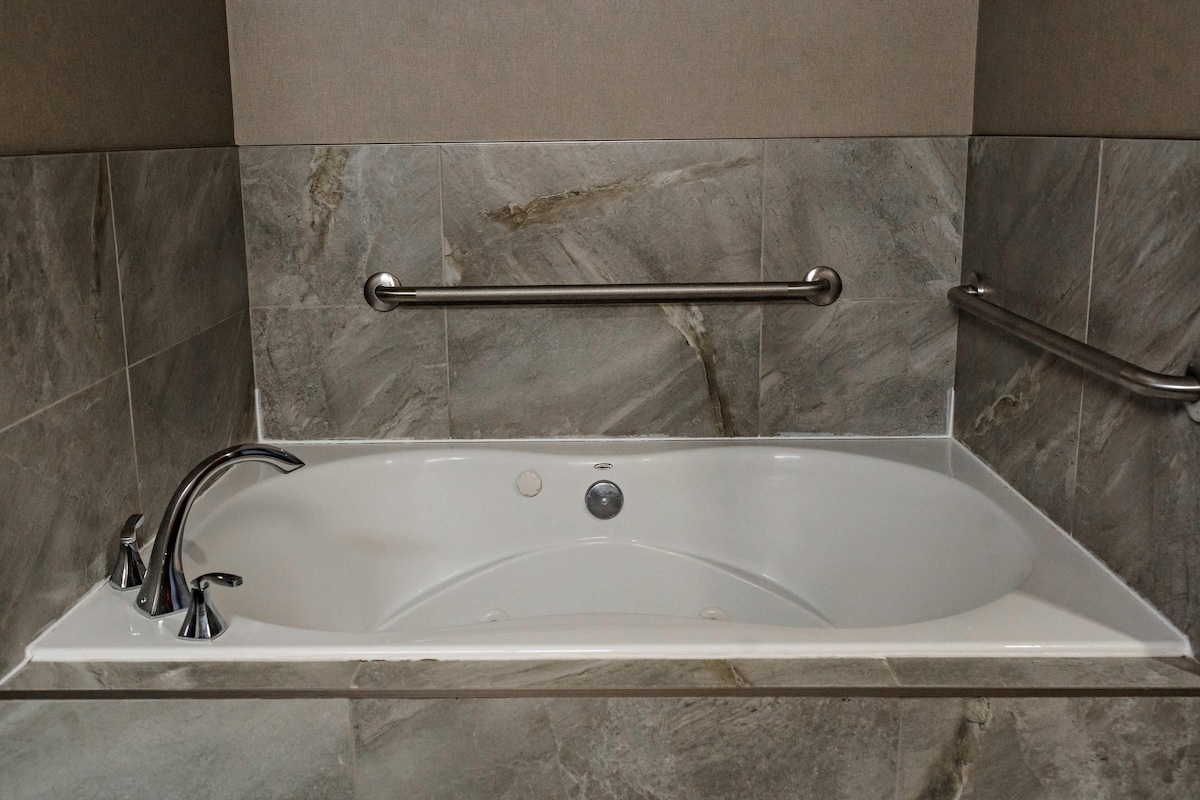A modern bathroom with a freestanding bathtub, grab bars, and marble tiles.