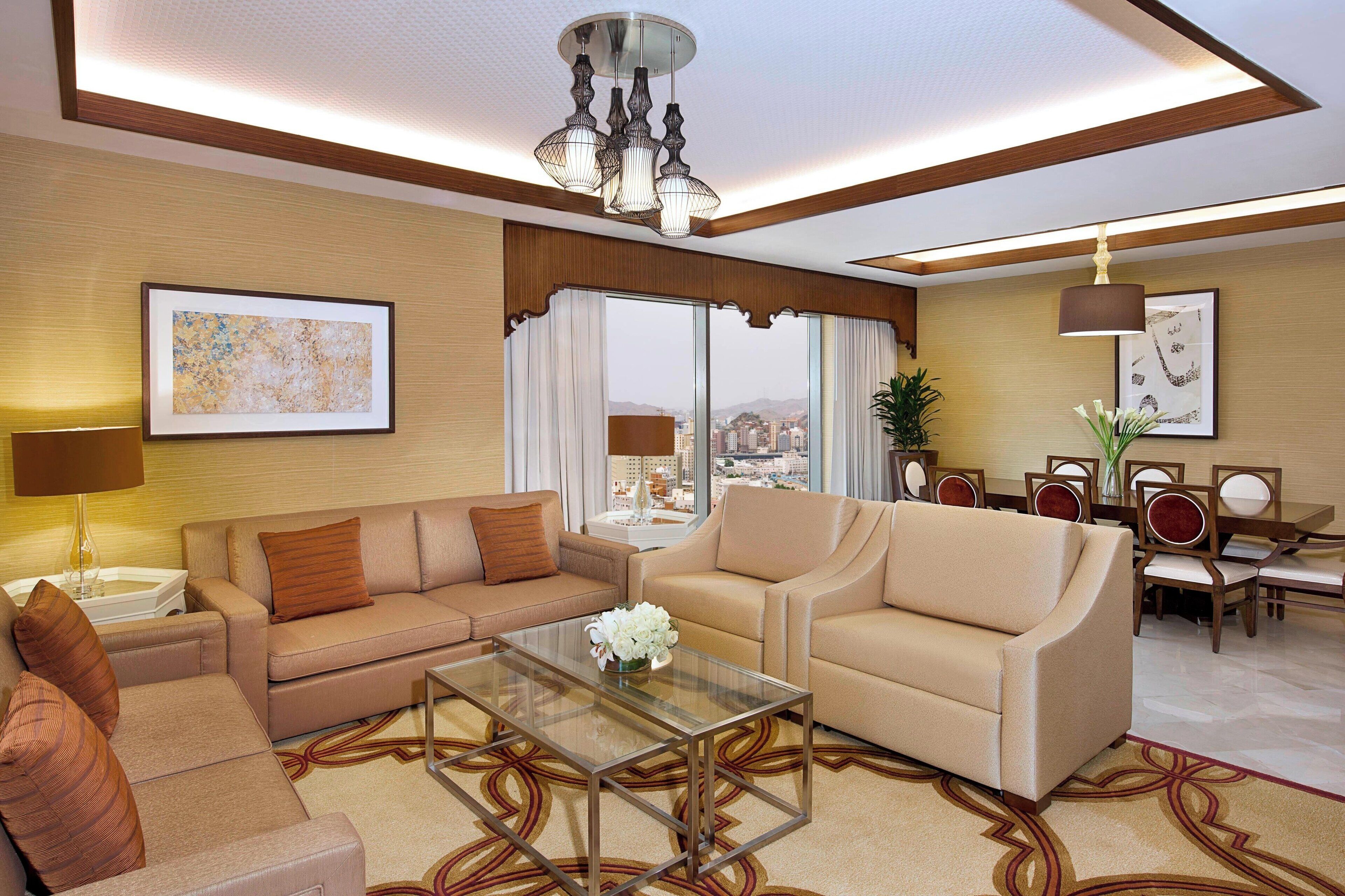 A modern hotel room with a sofa, armchair, and dining area.