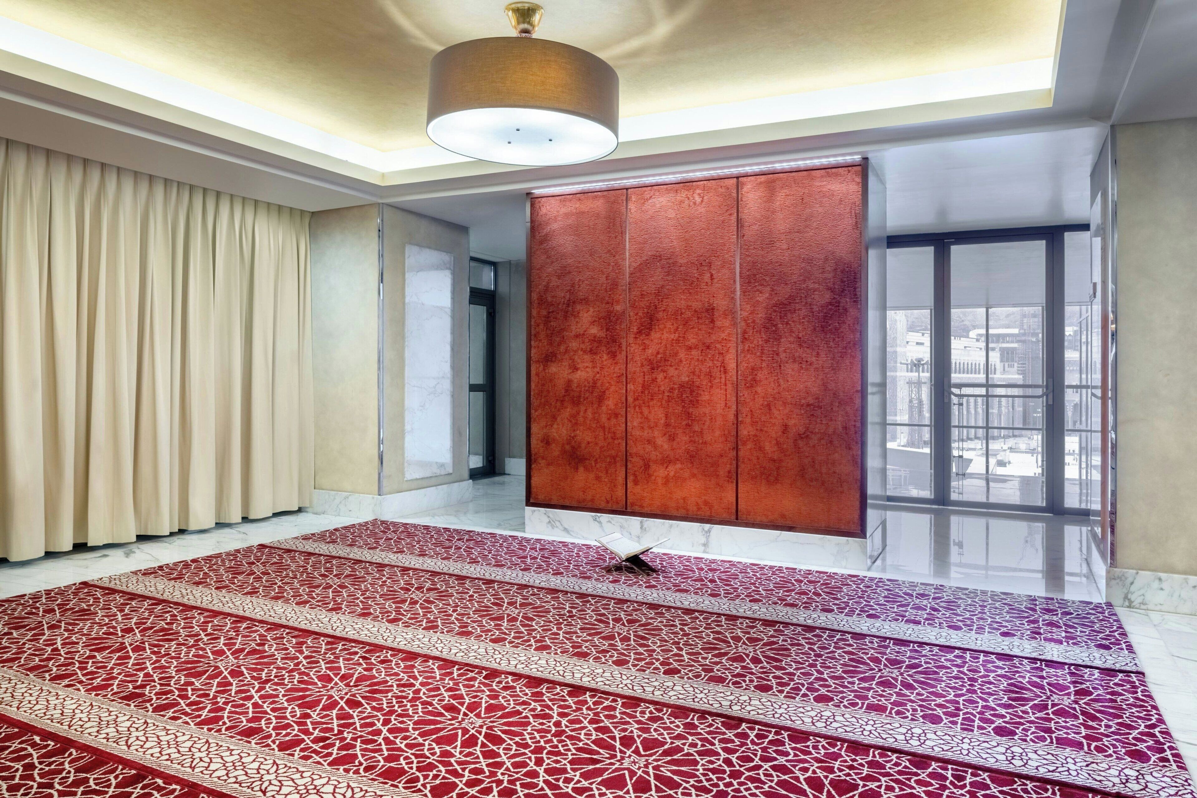 Una habitación amplia con una alfombra grande de estampado rojo, un armario de madera y vistas a través de un ventanal.