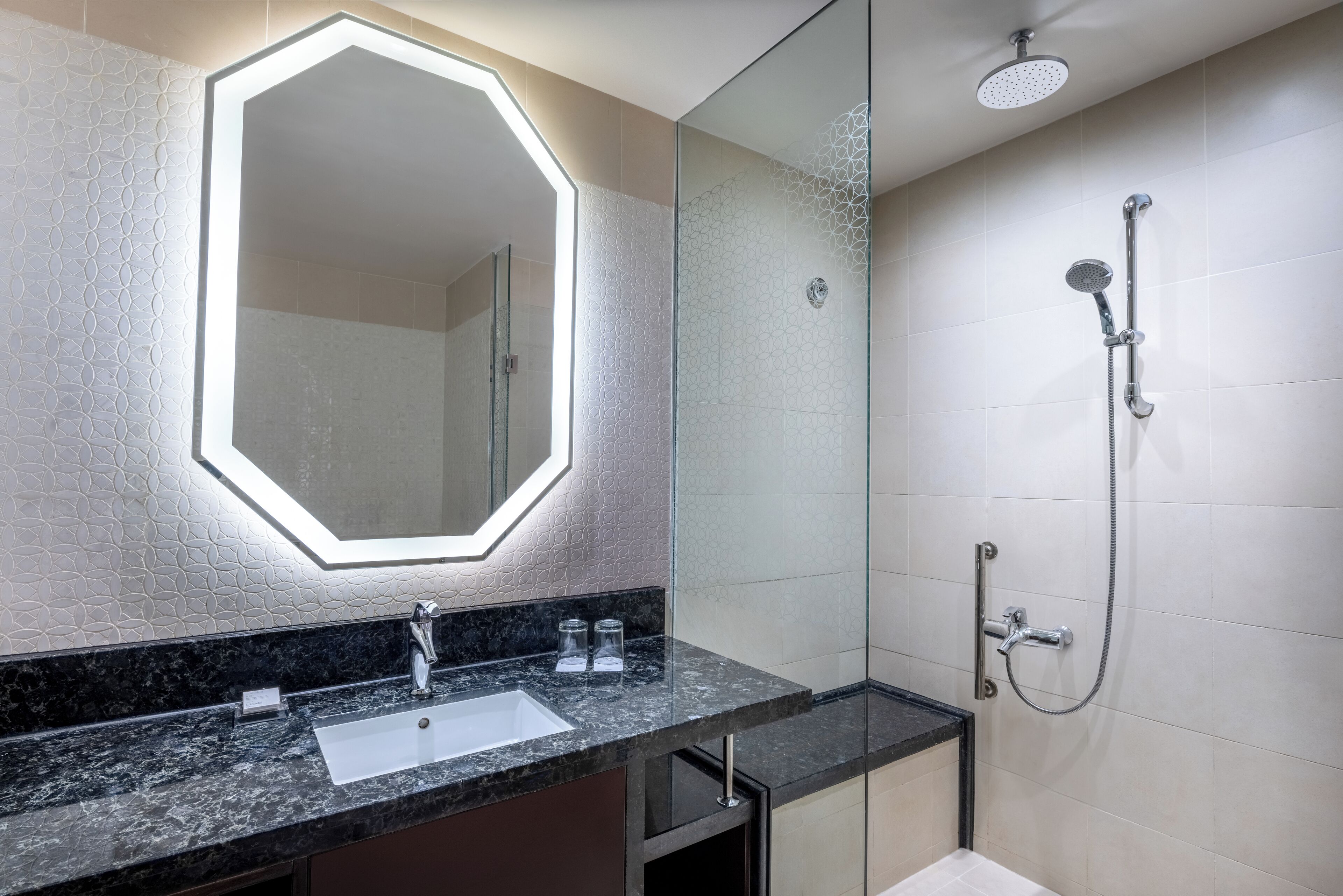 Un bagno moderno con cabina doccia in vetro, un ampio specchio con illuminazione geometrica e un piano di marmo.