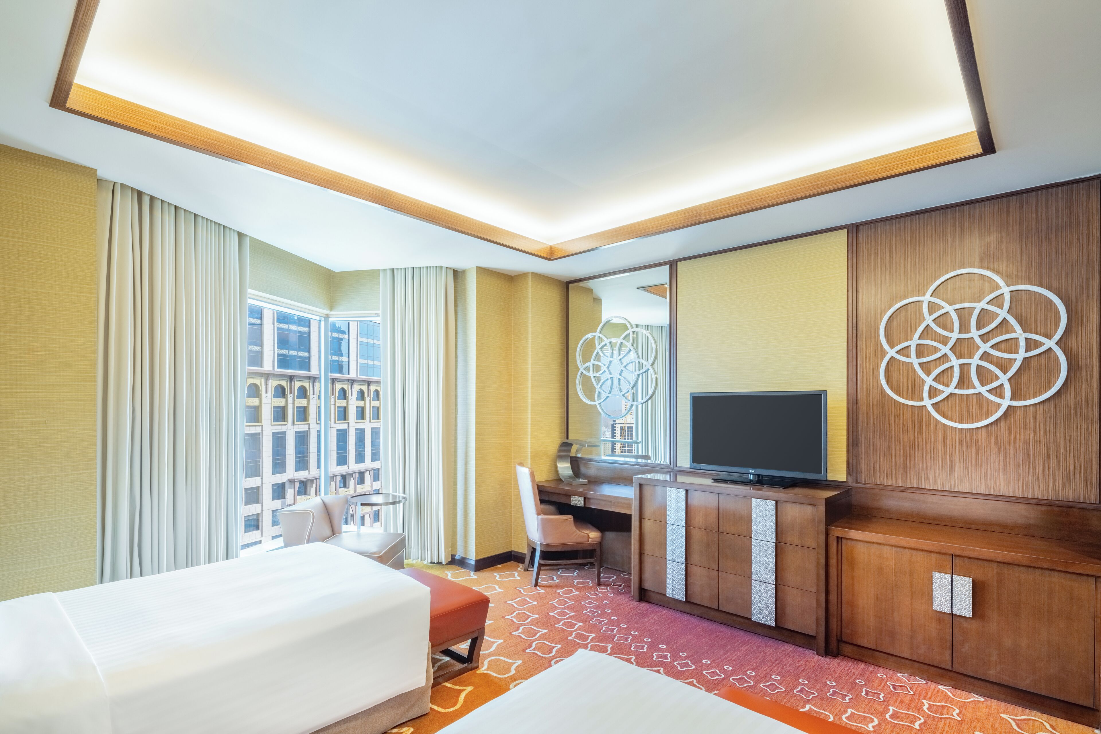 A hotel room with a bed, desk, chair, TV, and a large window with curtains.