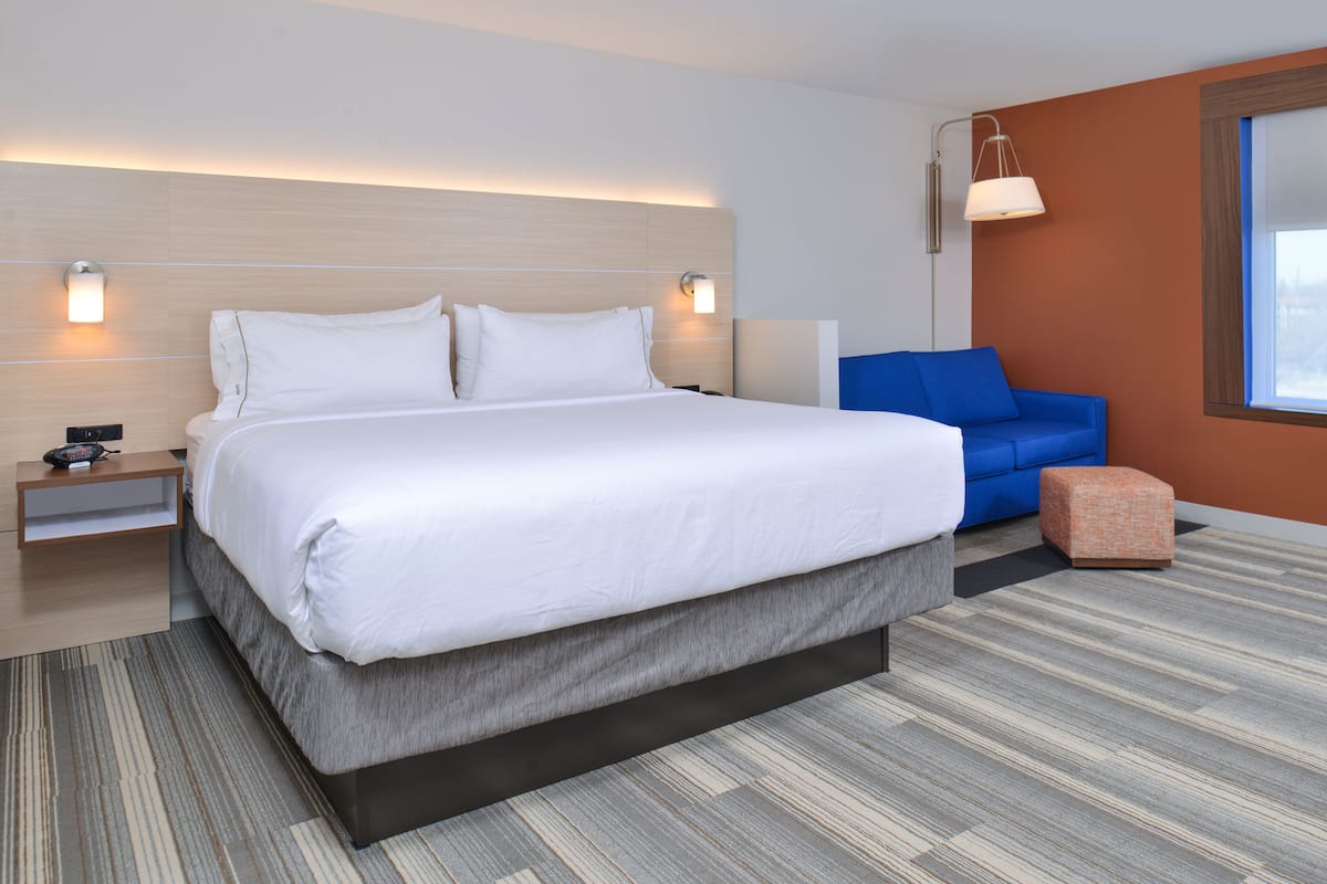 Camera d'albergo moderna con un letto grande, un divano blu, un poggiapiedi e un comodino con lampada.
