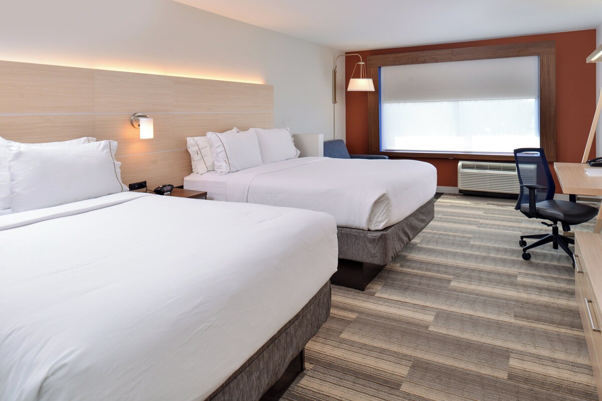 Hotelkamer met twee bedden, een bureau met stoel, een groot raam en een luchtverkoeler aan de muur.
