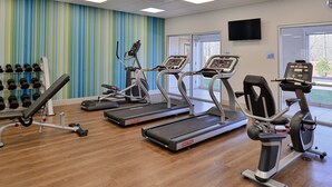 Un gimnasio con cintas de correr, mancuernas y una televisión en la pared.