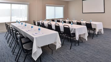 A conference room with long tables, chairs, water bottles, and a projector screen.