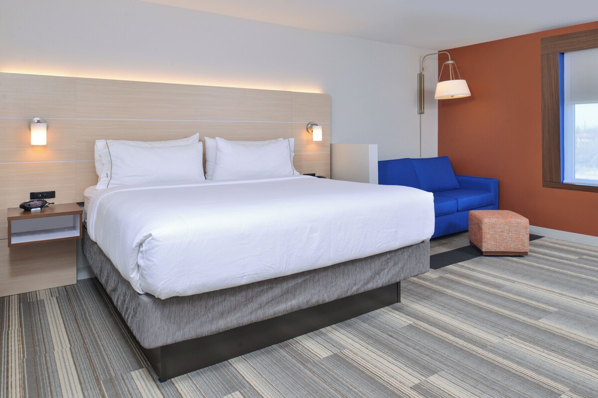 Een moderne hotelkamer met een groot bed, een blauwe bank, een klein voetenbankje en een nachtkastje.