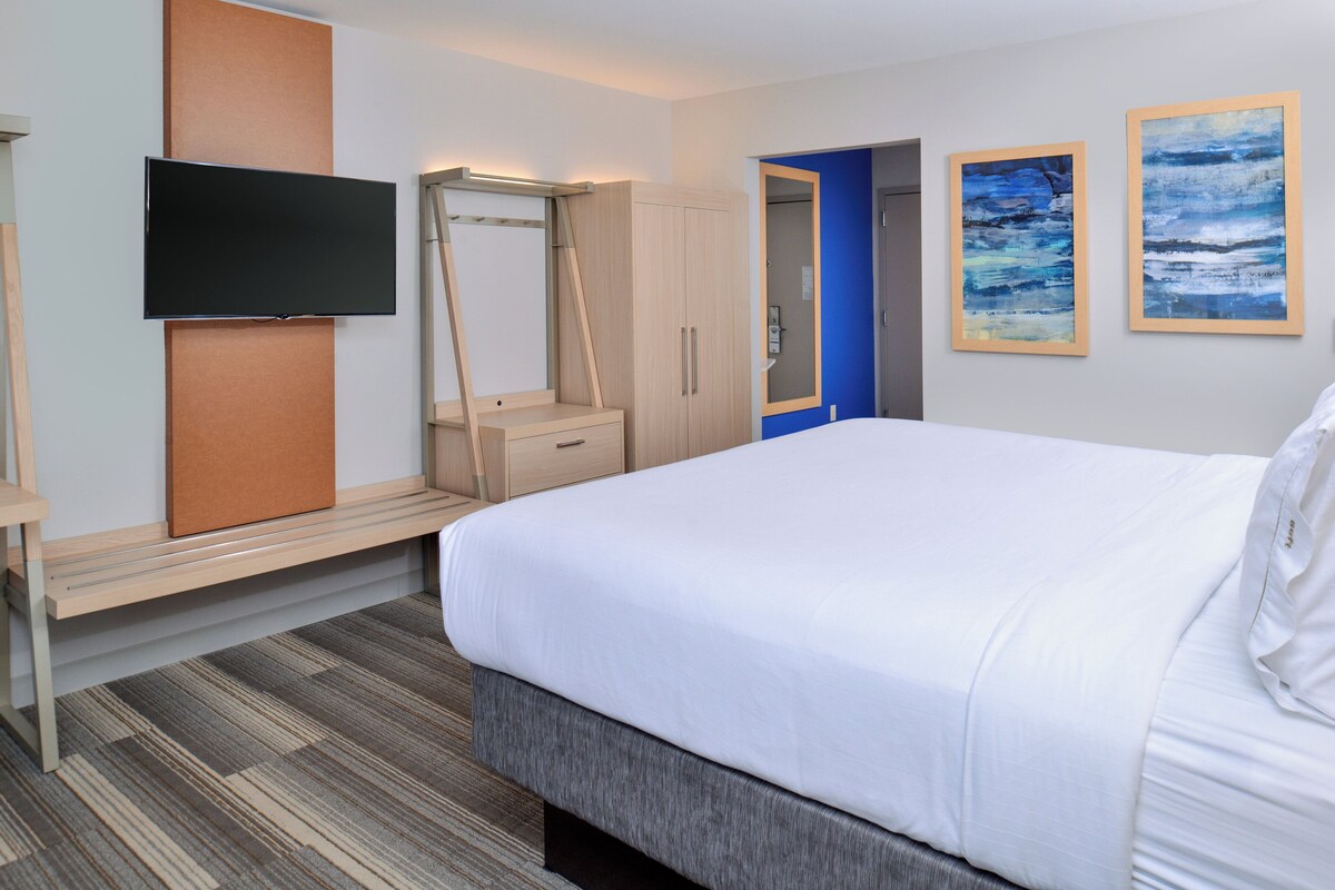 Een hotelkamer met een bed, een televisie, een kledingkast en twee ingelijste kunstwerken aan de muur.