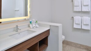 Moderni kylpyhuone, jossa on valkoinen pesuallas, puinen allaskaappi ja peili, jonka kehys on valaistu. Valkoiset pyyhkeet on ripustettu pyyhetelineeseen, ja taustalla näkyy wc-istuin.