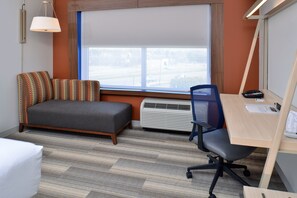 A hotel room with a bed, a desk, a chair, an air conditioner, and a window with a view of the outside.