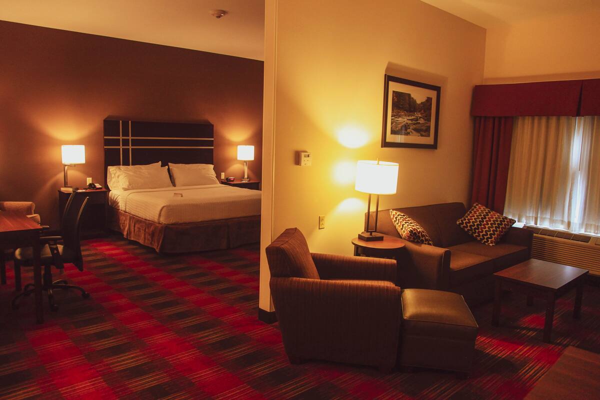 A hotel room with a bed, a sofa, a chair, a table, and a lamp.