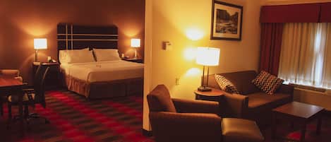Ett hotellrum med en säng, en soffa, en stol, ett bord och en lampa.