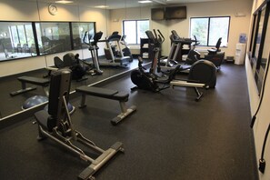 A gym with various exercise equipment, large windows, and a clock on the wall. - Holiday Inn Express & Suites Cumberland - La Vale by IHG (Cumberland)