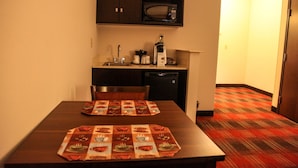 A small kitchenette with a microwave, coffee maker, and sink. There is a table with a placemat and a chair. The floor has a patterned carpet. - Holiday Inn Express & Suites Cumberland - La Vale by IHG (Cumberland)
