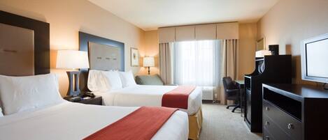 A hotel room with two beds, a desk, a chair, a television, and a window with curtains.