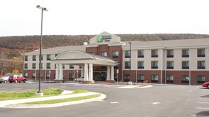A Holiday Inn Express building with a covered entrance, parking lot, and a hilly background. - Holiday Inn Express & Suites Cumberland - La Vale by IHG (Cumberland)