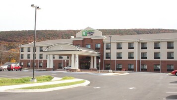 Edifício Holiday Inn Express com entrada coberta, estacionamento e paisagem montanhosa ao fundo.