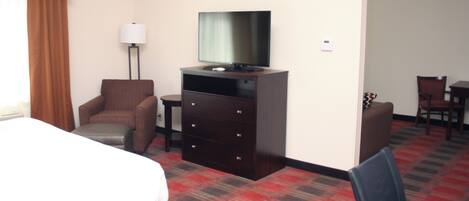 Habitación de hotel con cama, cómoda con televisor, una silla, escritorio y lámpara.