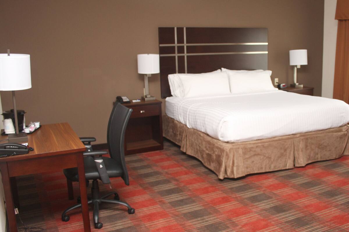 A hotel room with a large bed, a desk with a chair, a telephone, and two lamps.