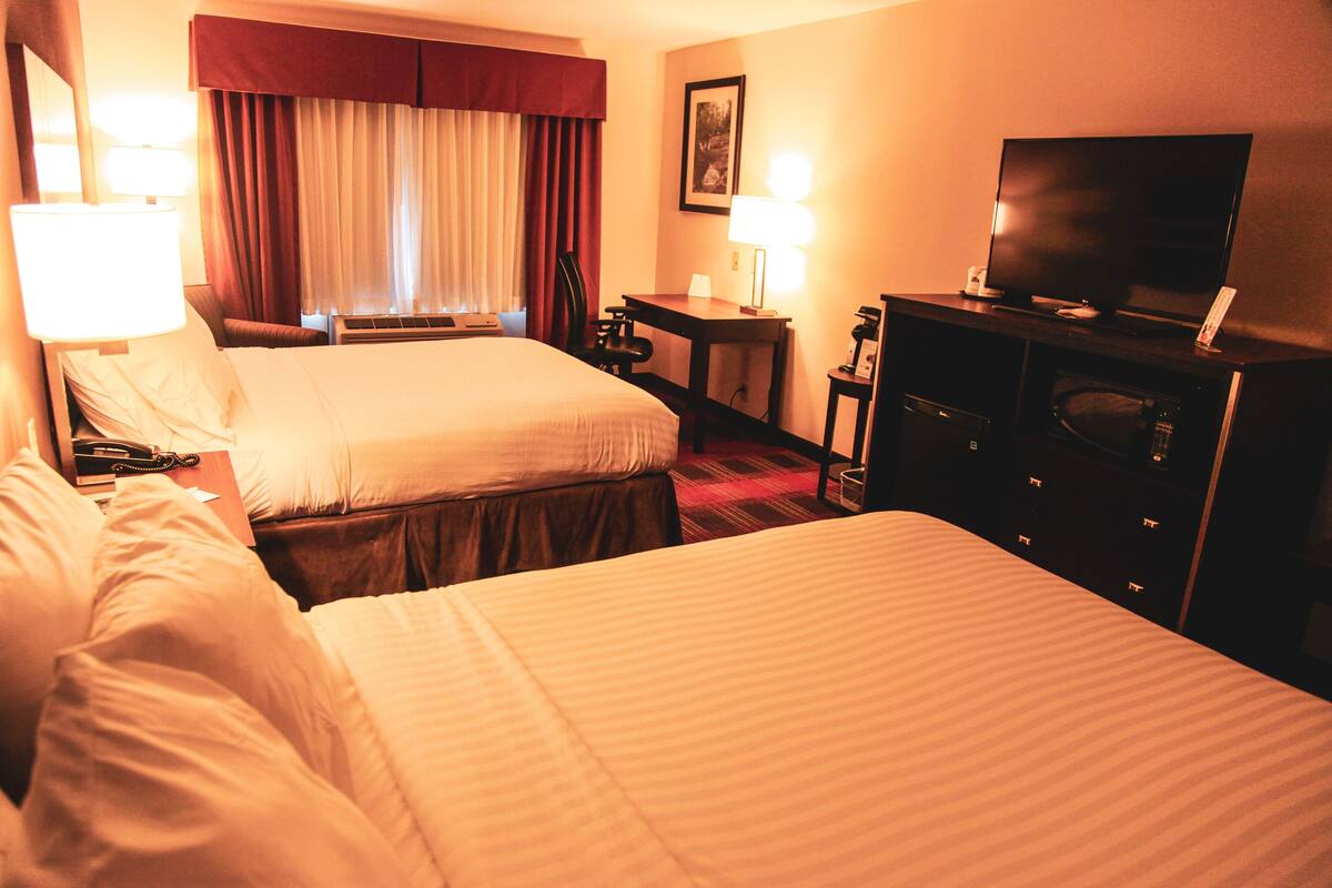 A hotel room with two beds, a desk, a television, and a window with curtains.