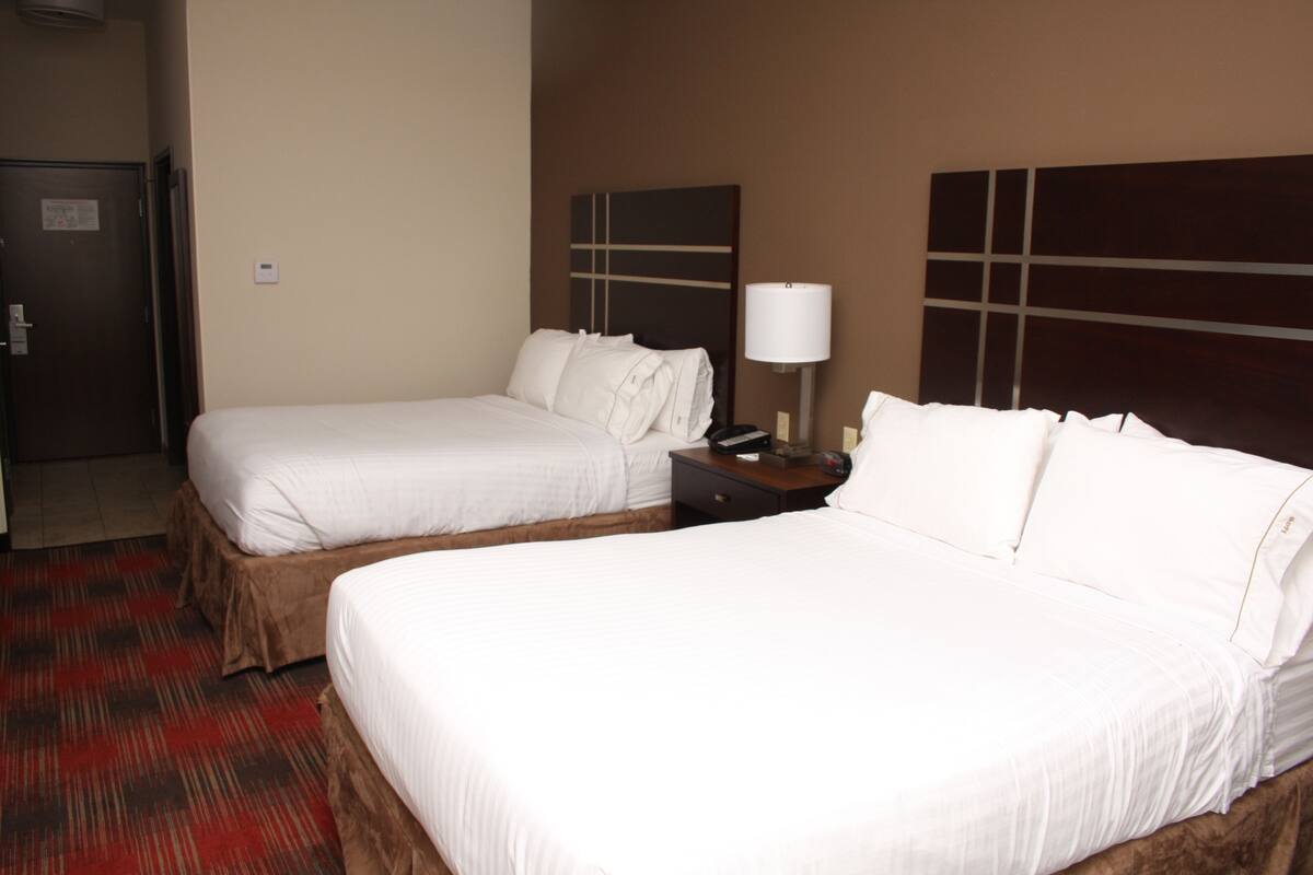A hotel room with two single beds, a nightstand with a lamp, and a red carpeted floor.