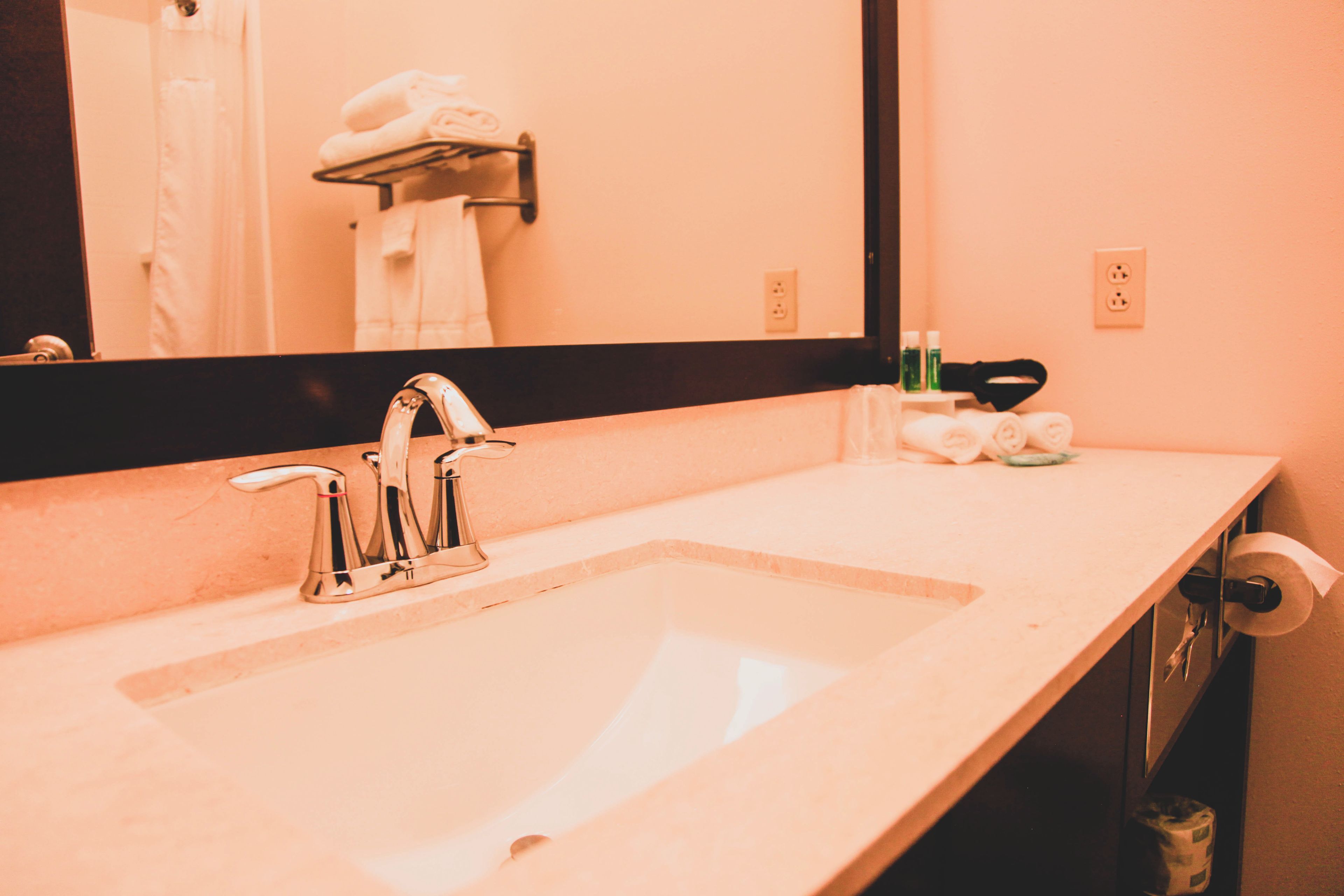 Un baño con lavamanos, espejo, toallero y artículos de aseo.