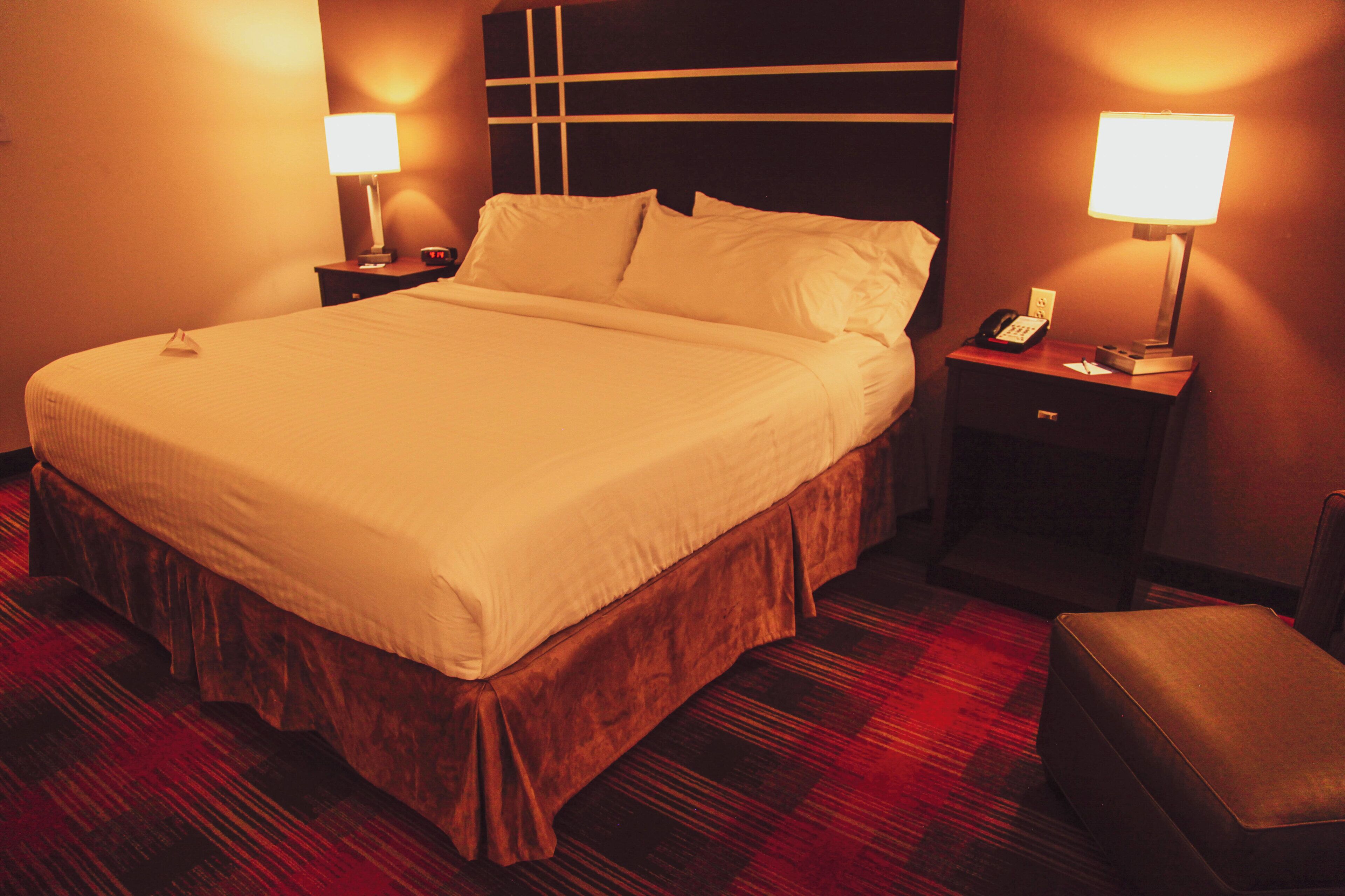 Una habitación de hotel con una cama grande, dos mesitas de noche, un sillón y suelo alfombrado.