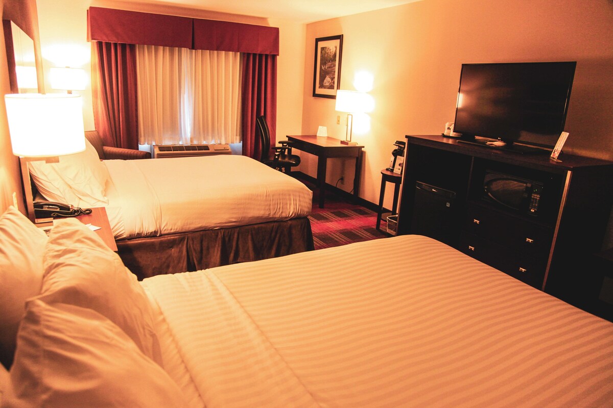 A hotel room with two beds, a television, a desk, and a chair.