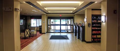 A hotel lobby with a reception desk, a vending machine, and a seating area with chairs.