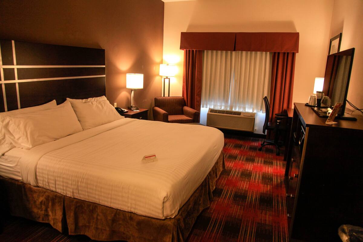 A hotel room with a large bed, a desk, a chair, a lamp, and a window with curtains.