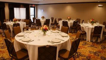 A banquet hall with round tables set for dining, each with white tablecloths, chairs, and floral centerpieces.