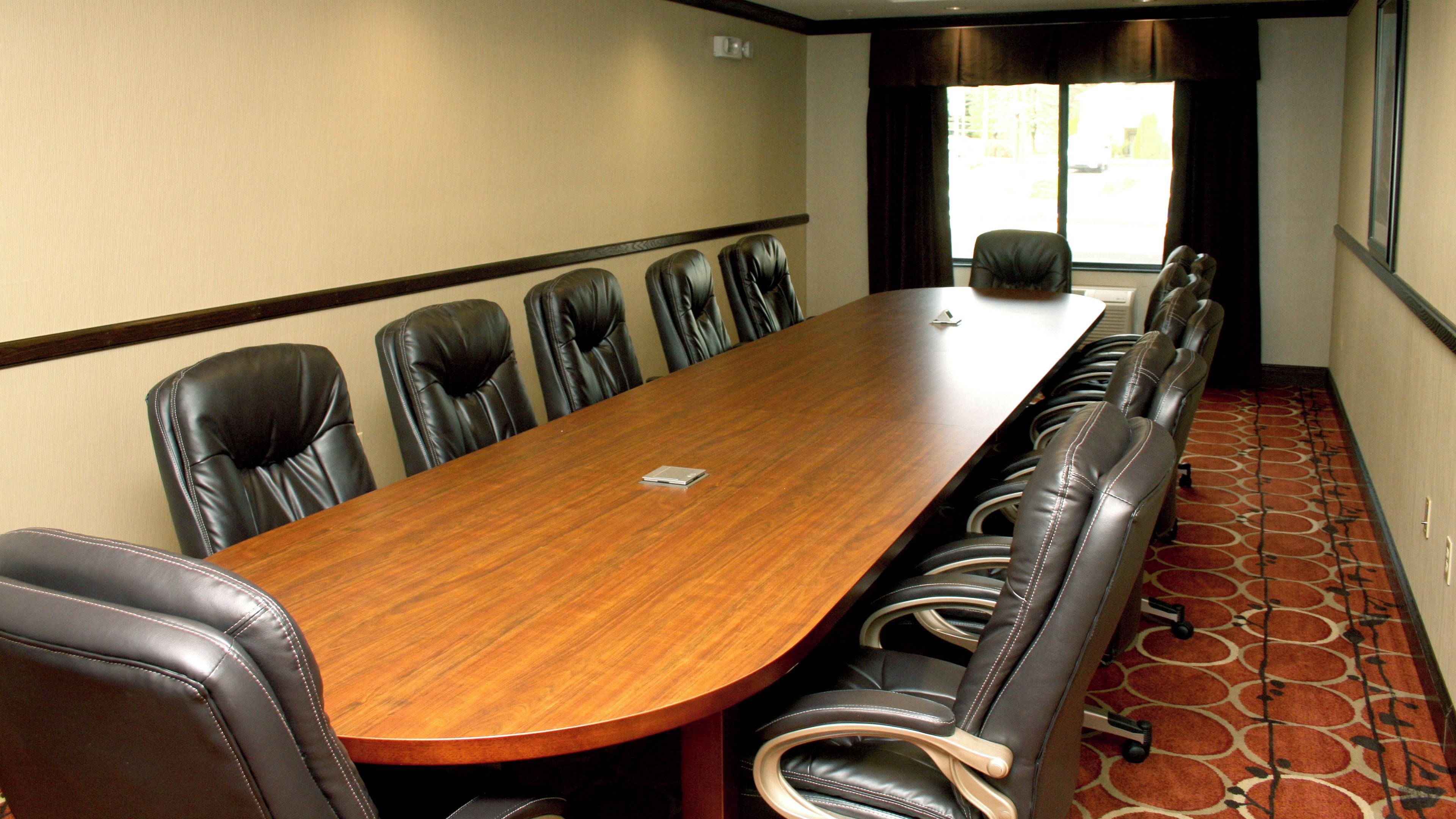A conference room with a long wooden table and multiple leather chairs.